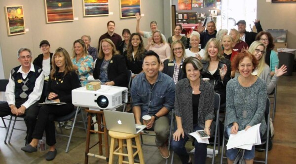 Large group of people gathered in an office space smiling at the camera in front of a projector.