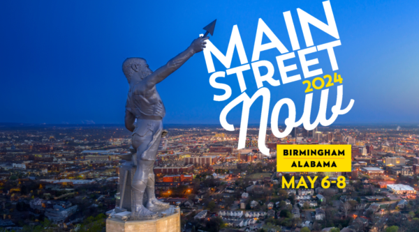 Vulcan Statue with illuminated city of Birmingham skyline in the background. The statue's raised spear points to the Main Street Now 2024 logo in the upper right corner.