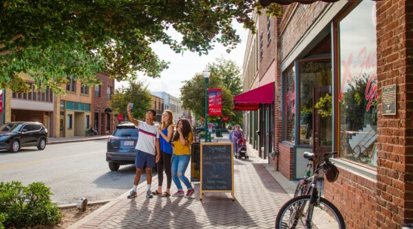 People pose for a selfie on a sunlit downtown street