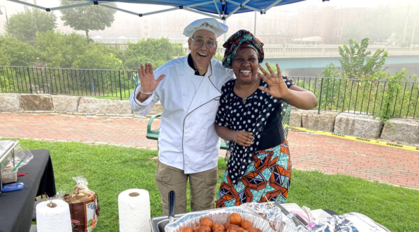 Two vendors pose at the Cultural Cuisines tent during the River Jam event in Biddeford, Maine