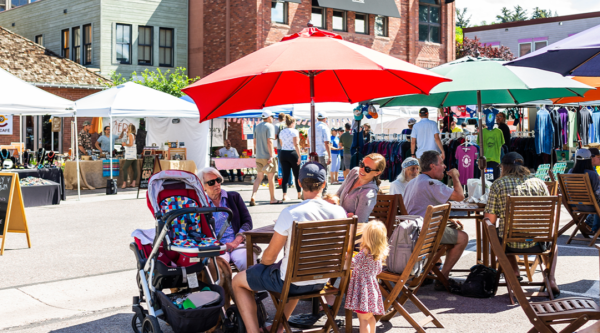 People sitting at tables and browsing stalls at an open streets event