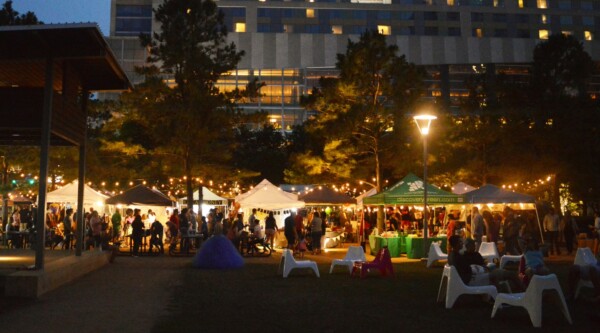 People sit at outdoor tables and shop at tents during a market in Discovery Green Park, Houston, Texas.