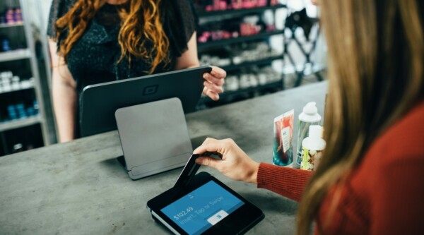 A woman stands at a cash register while another woman inserts her credit card into a payment machine