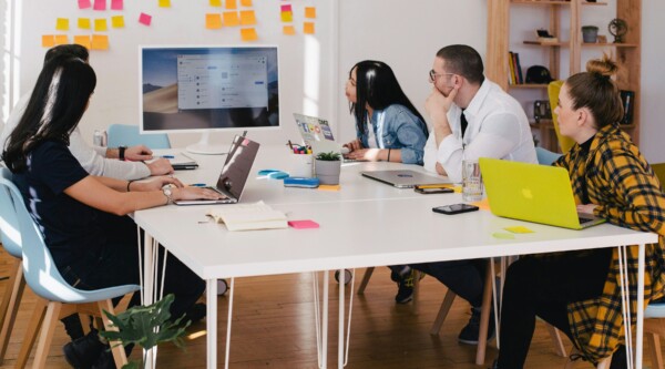 People sitting around a table with laptops looking at a board with sticky notes