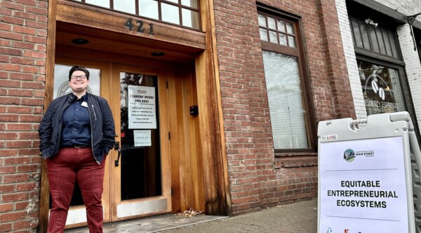 Tasha Sams poses in front of a brick building next to a sign reading "equitable entrepreneurial ecosystems"