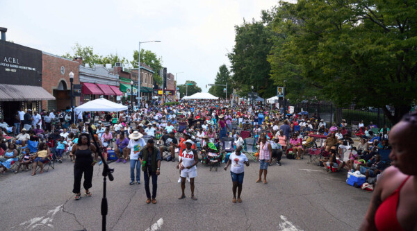 Street lined with storefronts and filled with people enjoying a concert.