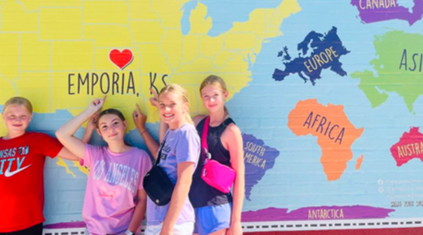 Four pre-teen girls post in front of a downtown mural featuring a map of the US