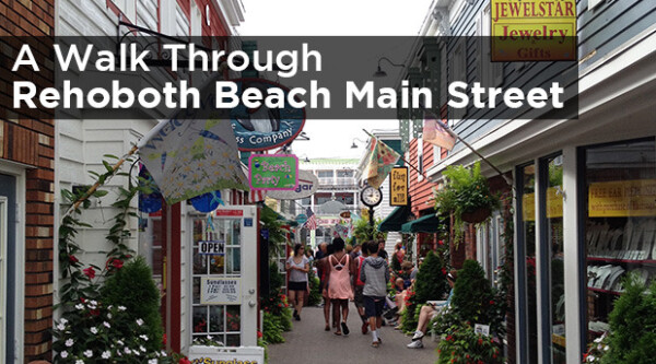 People walking along narrow sidewalk with small businesses along each side.