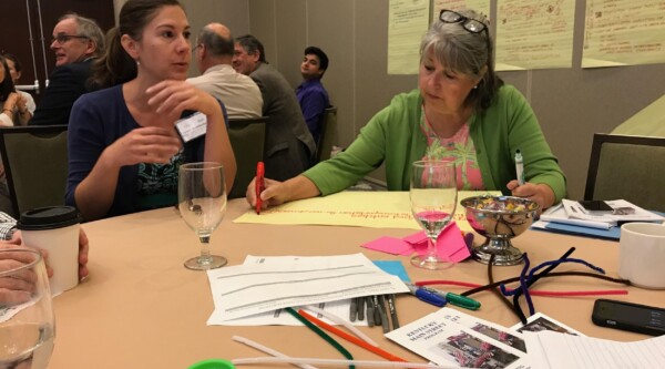 Women sit at a round table having a conversation and taking notes.