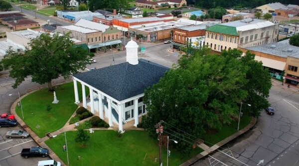 White stately building with columns and tower at the center of a town square.