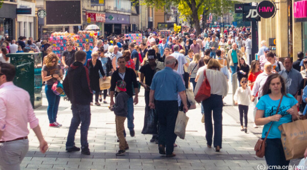 Large crowd of people walk through commercial district