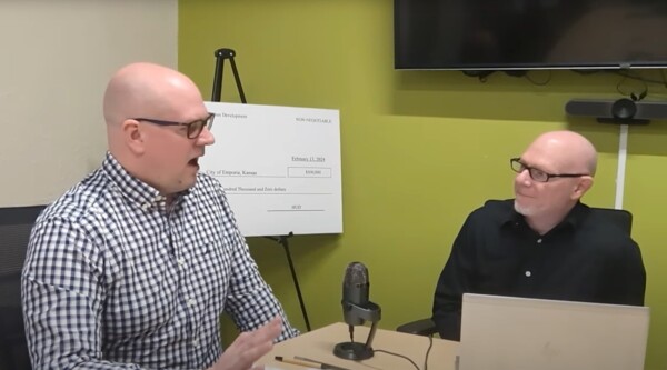 Two professional men sit in office in front of microphone.