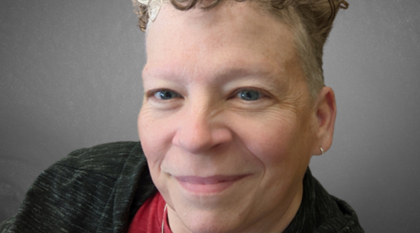 Headshot of woman with white hair wearing blue and black shirt.