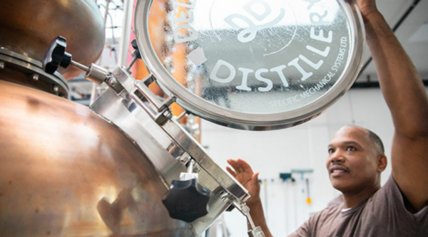 Man wearing brown t-shirt opens door to distilling equipment.