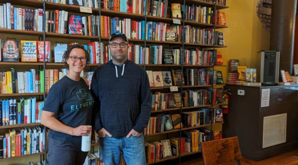 Man and woman stand in front of bookcase in small business.