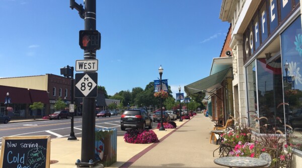 Streetscape with outdoor dining, storefronts, lamp posts, and flowers.