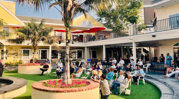 People attending an outdoor meeting sit in shade created by trees and awnings