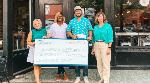 A group of people holding a large award check in front of a downtown storefront