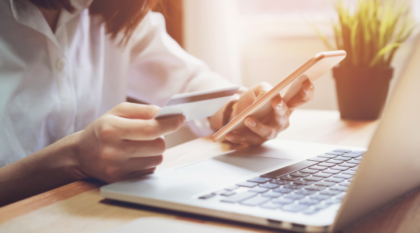 A woman sitting at a table with a laptop holding a cell phone and credit card