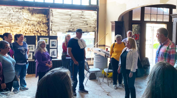 A group of people in a room during an in-progress renovation listen to a man presenting information