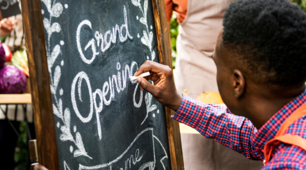 Man writing Grand Opening on a chalkboard outside a small business.